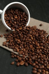 Photo of Aromatic coffee beans and overturned cup on black table, closeup