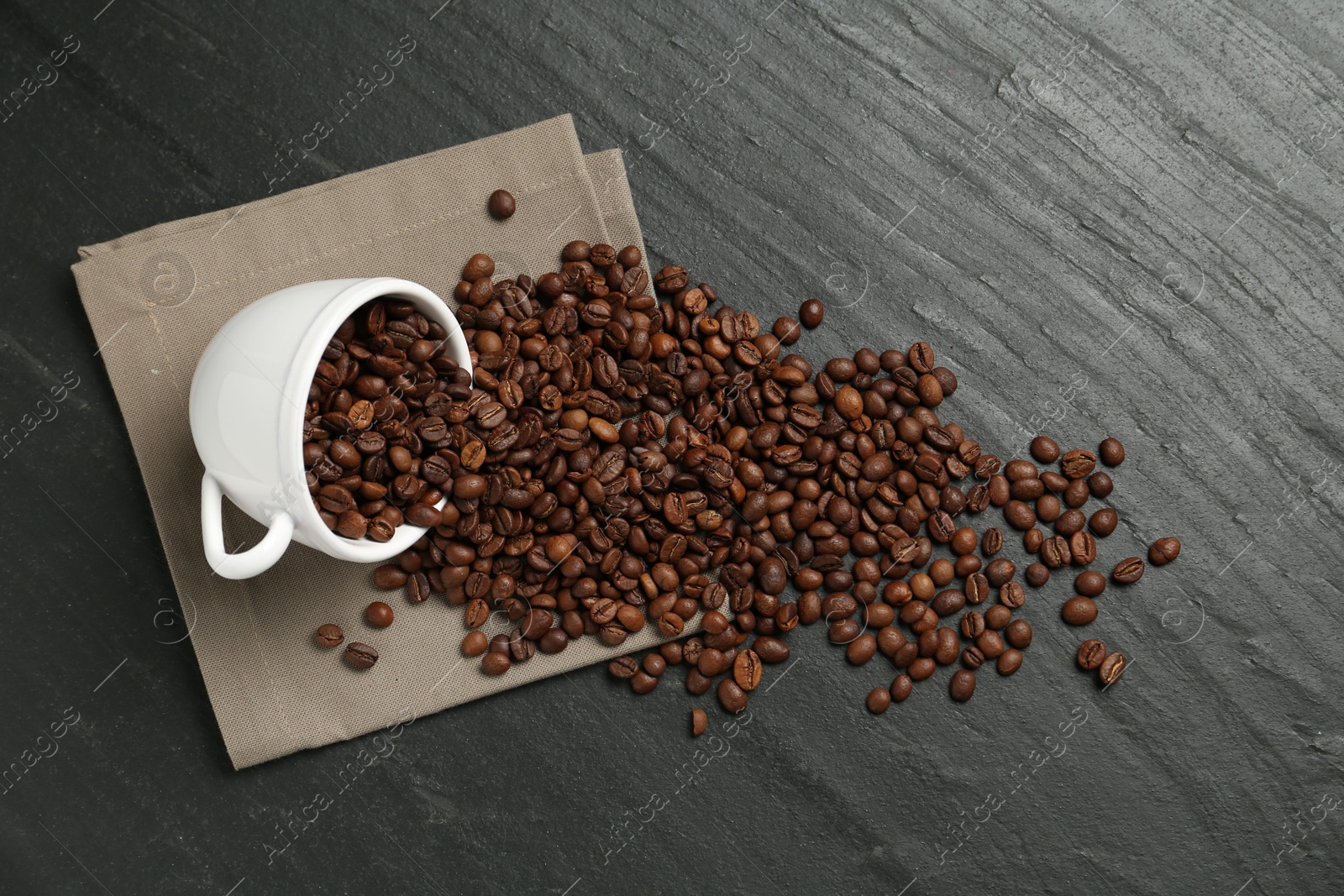 Aromatic coffee beans and overturned cup on black table, flat lay Photo of Aromatic coffee beans and overturned cup on black table, flat lay
