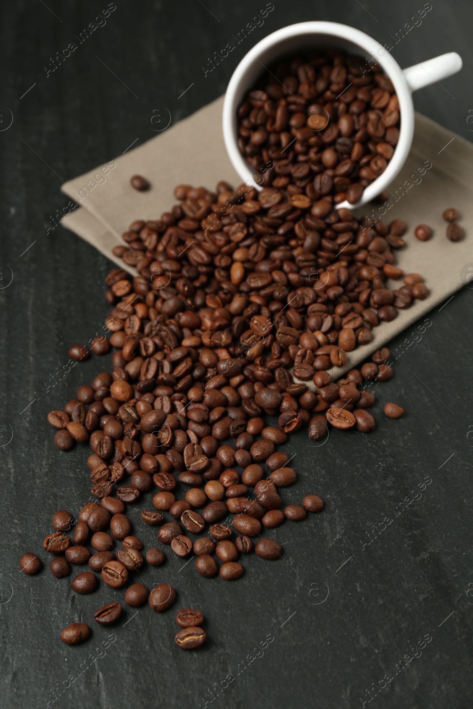 Aromatic coffee beans and overturned cup on black table, closeup Photo of Aromatic coffee beans and overturned cup on black table, closeup