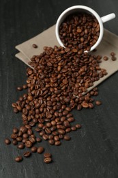 Photo of Aromatic coffee beans and overturned cup on black table, closeup