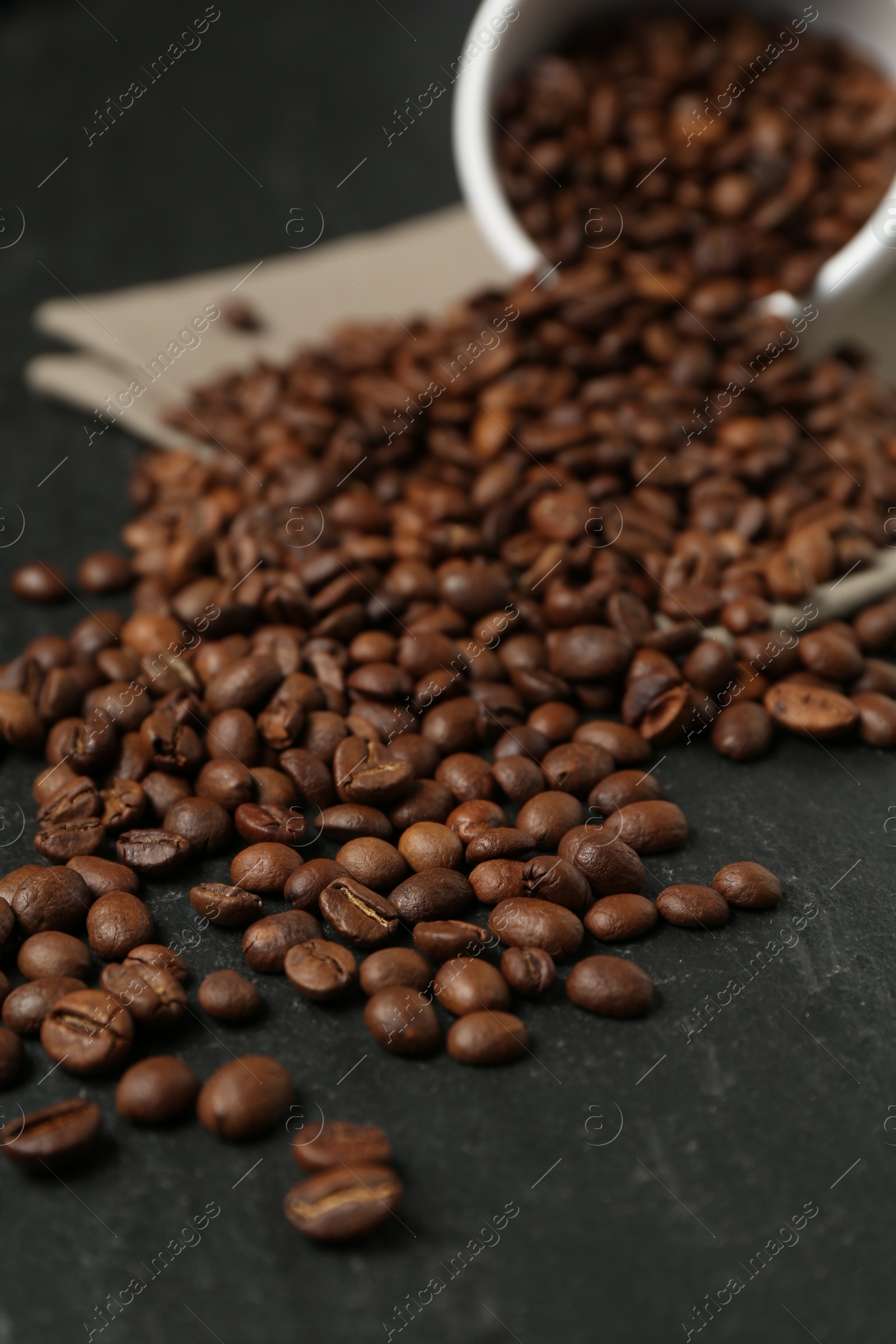 Aromatic coffee beans and overturned cup on black table, closeup Photo of Aromatic coffee beans and overturned cup on black table, closeup