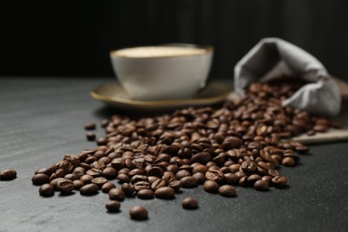 Photo of Aromatic coffee beans and hot drink on black table, closeup