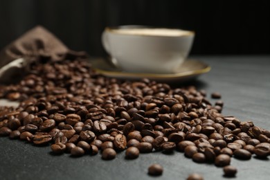 Photo of Aromatic coffee beans and hot drink on black table, closeup