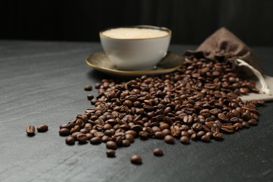 Photo of Aromatic coffee beans and hot drink on black table, closeup