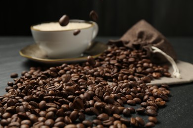 Photo of Aromatic coffee beans and hot drink on black table, closeup