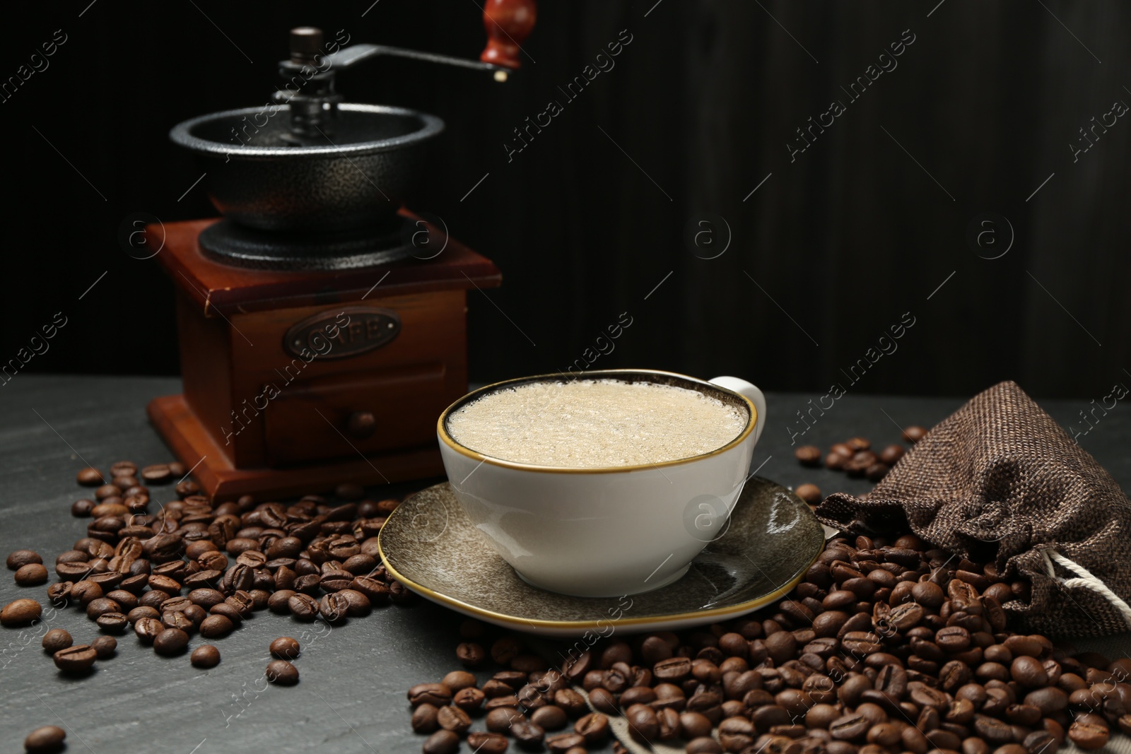Aromatic coffee in cup, beans and grinder on black table Photo of Aromatic coffee in cup, beans and grinder on black table