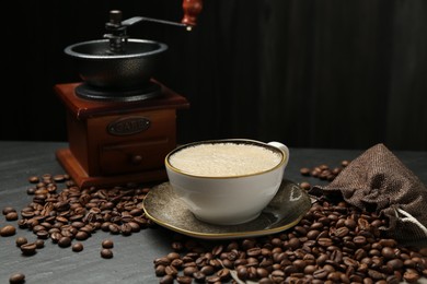 Photo of Aromatic coffee in cup, beans and grinder on black table