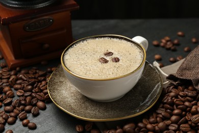Photo of Aromatic coffee in cup, beans and grinder on black table, closeup