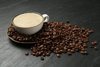 Photo of Aromatic coffee in cup and beans on black table, closeup