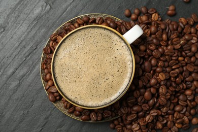 Photo of Aromatic coffee in cup and beans on black table, flat lay