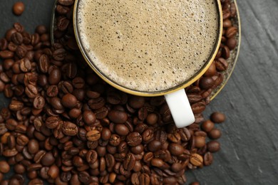 Photo of Aromatic coffee in cup and beans on black table, flat lay