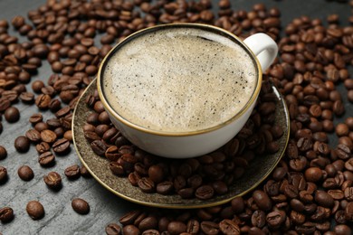 Photo of Aromatic coffee in cup and beans on black table, closeup