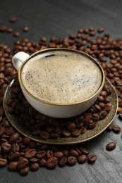 Photo of Aromatic coffee in cup and beans on black table, closeup