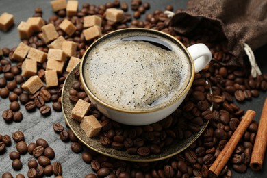 Photo of Aromatic coffee in cup, beans, brown sugar and cinnamon on black table, closeup