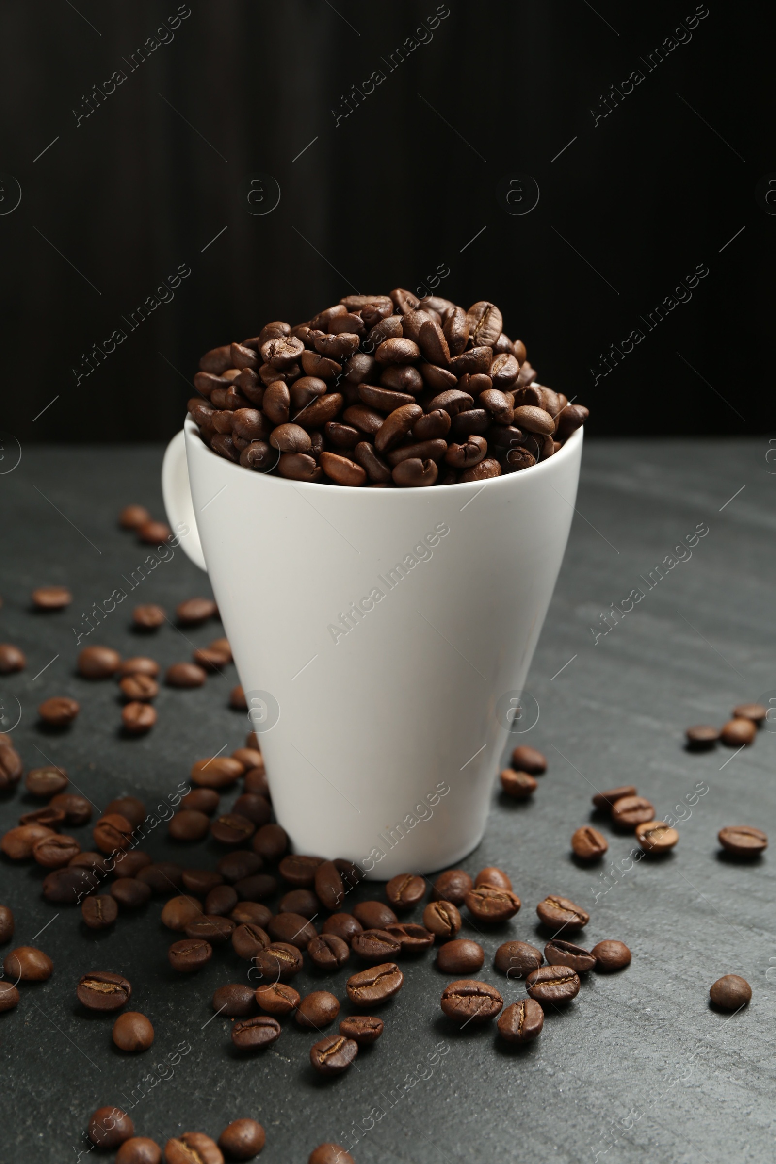 Aromatic coffee beans in cup on black table, closeup Photo of Aromatic coffee beans in cup on black table, closeup