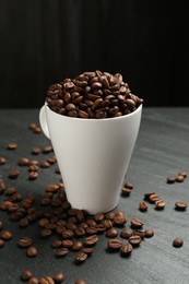 Photo of Aromatic coffee beans in cup on black table, closeup