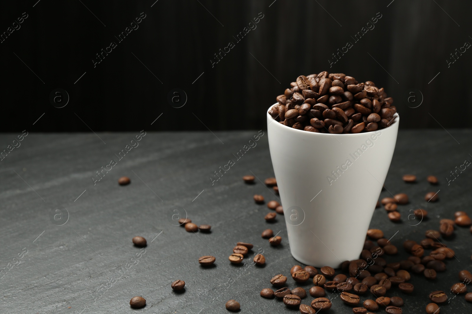 Aromatic coffee beans in cup on black table, closeup. Space for text Photo of Aromatic coffee beans in cup on black table, closeup. Space for text
