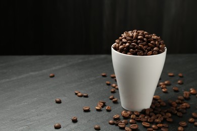 Photo of Aromatic coffee beans in cup on black table, closeup. Space for text