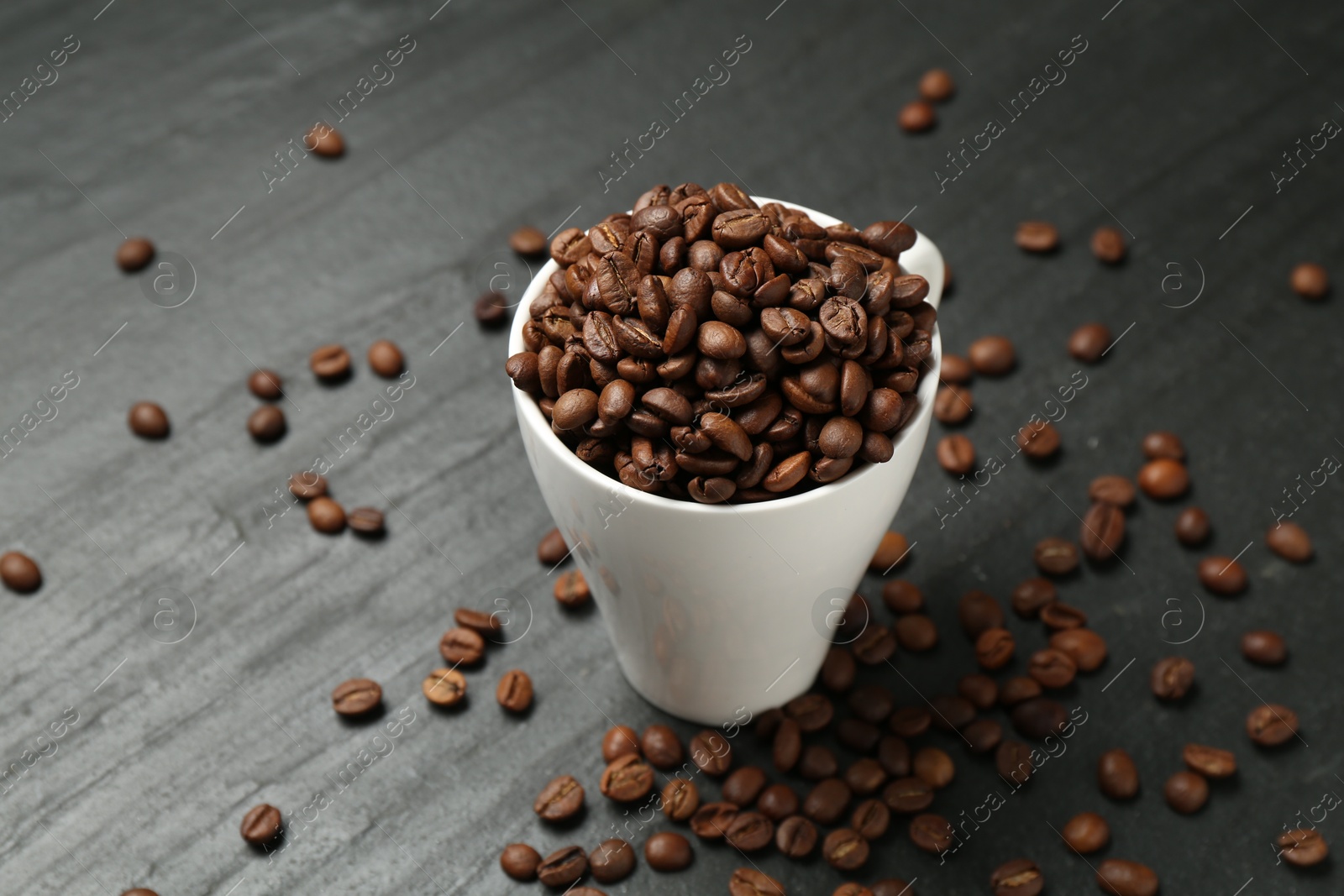 Aromatic coffee beans in cup on black table, closeup Photo of Aromatic coffee beans in cup on black table, closeup