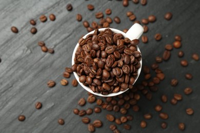Photo of Aromatic coffee beans in cup on black table, flat lay