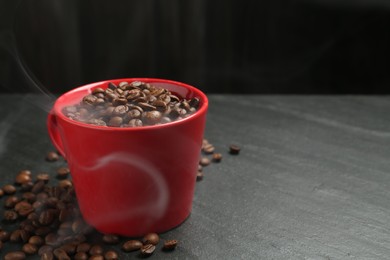 Photo of Aromatic coffee beans in cup on black table, closeup. Space for text