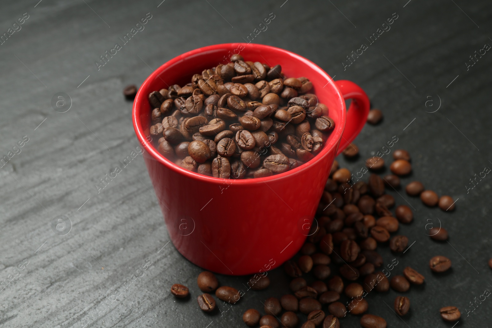 Aromatic coffee beans in cup on black table, closeup Photo of Aromatic coffee beans in cup on black table, closeup