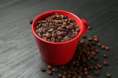 Photo of Aromatic coffee beans in cup on black table, closeup