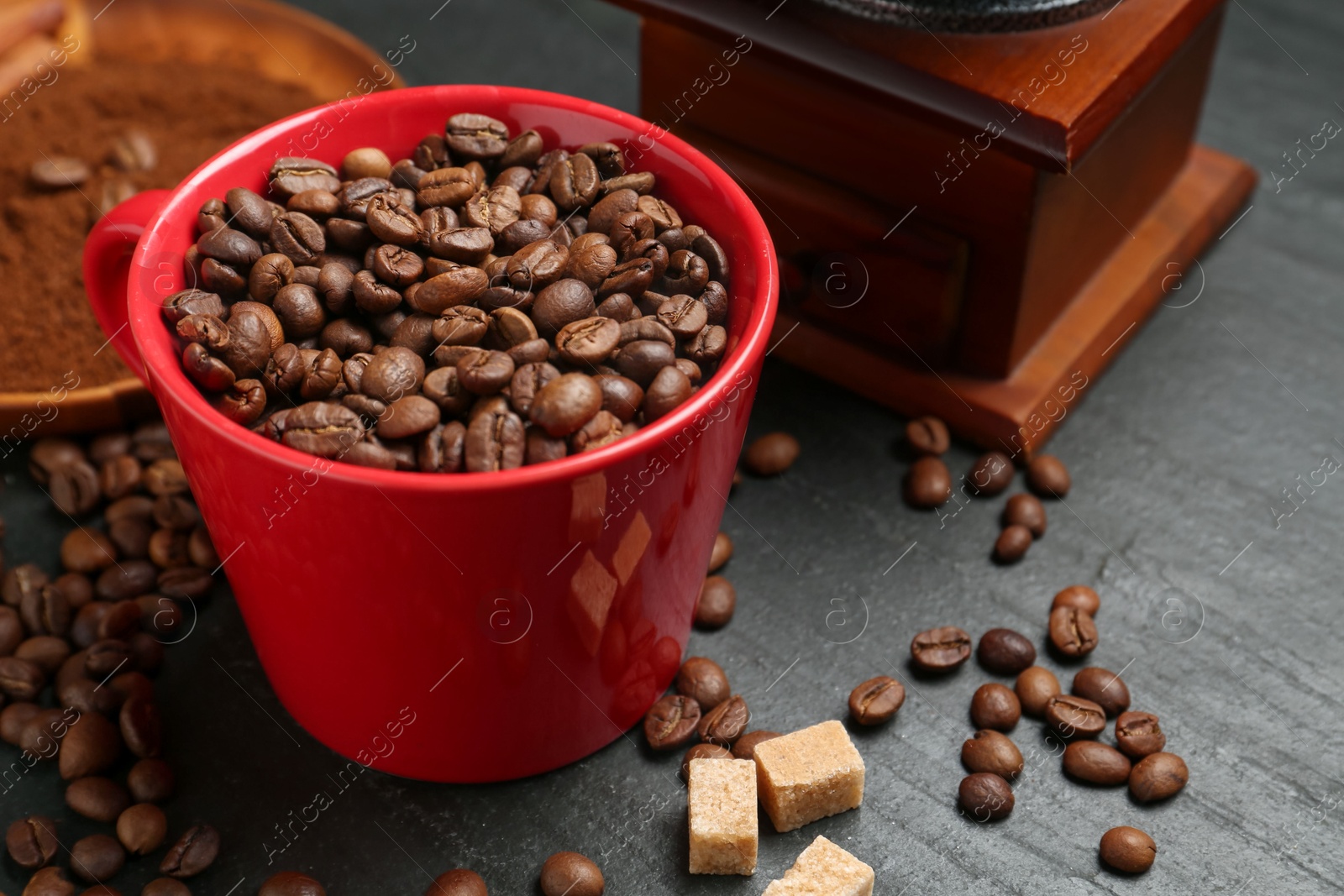 Aromatic coffee beans in cup, grinder and brown sugar on black table, closeup Photo of Aromatic coffee beans in cup, grinder and brown sugar on black table, closeup