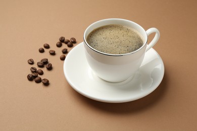 Photo of Aromatic coffee in cup and beans on beige background, closeup