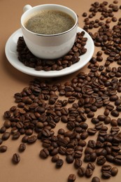 Photo of Aromatic coffee in cup and beans on beige background, closeup