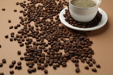 Photo of Aromatic coffee in cup and beans on beige background, closeup