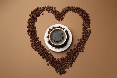 Photo of Aromatic coffee in cup and heart shaped of beans on beige background, flat lay