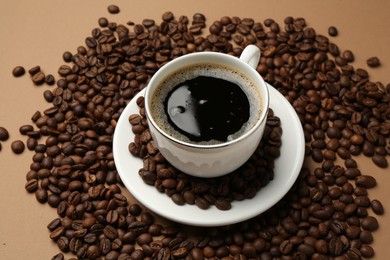 Photo of Aromatic coffee in cup and beans on beige background, above view