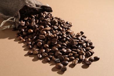 Photo of Aromatic coffee beans and sack on beige background, closeup