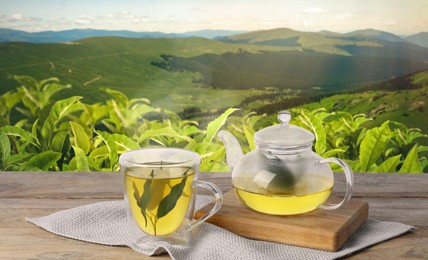 Image of Green tea in cup and teapot on wooden table against tea plantation in mountains. Banner design