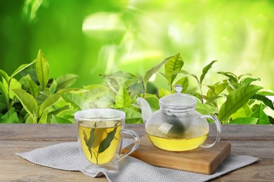 Image of Green tea in cup and teapot on wooden table in tea plantation