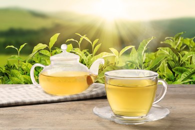 Image of Green tea in cup and teapot on wooden table against tea plantation in mountains