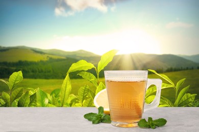 Image of Cup of green tea on white table against tea plantation in mountains. Space for text