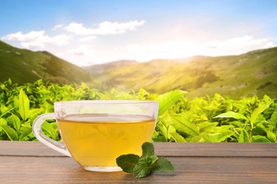 Image of Cup of green tea on wooden table against tea plantation in mountains. Space for text