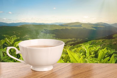 Image of Cup of green tea on wooden table against tea plantation in mountains. Space for text