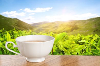 Image of Cup of green tea on wooden table against tea plantation in mountains. Space for text