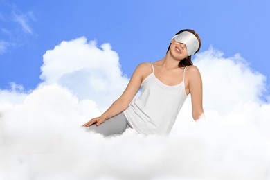 Image of Woman with sleep mask on fluffy cloud in blue sky. Bedtime