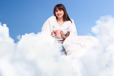 Image of Happy woman with blanket and cup of drink on fluffy cloud in blue sky