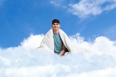Image of Happy man with blanket and sleep mask sitting on fluffy cloud in blue sky. Bedtime