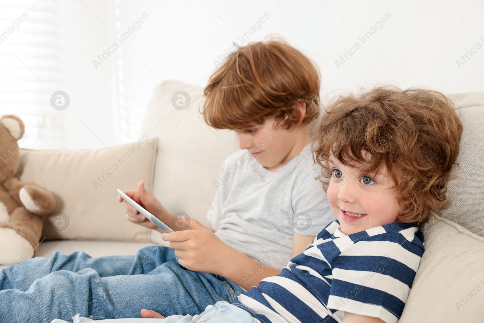 Cute little brothers with tablet on sofa at home Photo of Cute little brothers with tablet on sofa at home