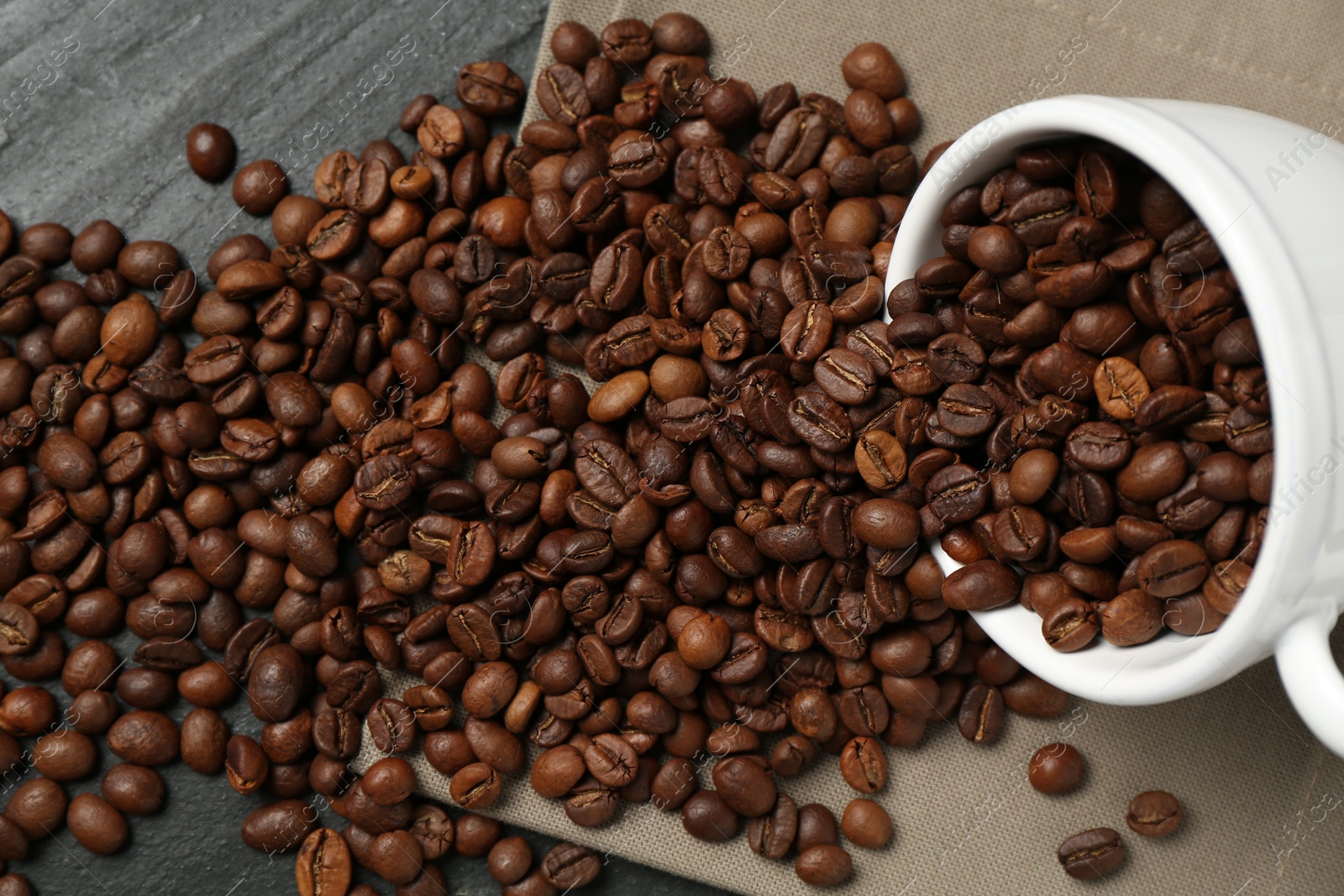 Aromatic coffee beans and overturned cup on black table, above view Photo of Aromatic coffee beans and overturned cup on black table, above view