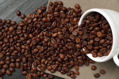 Photo of Aromatic coffee beans and overturned cup on black table, above view