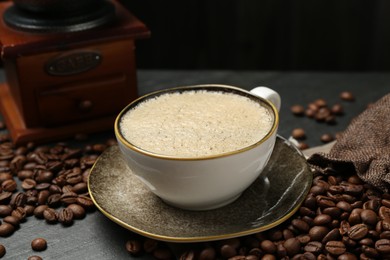 Photo of Aromatic coffee in cup, beans and grinder on black table, closeup