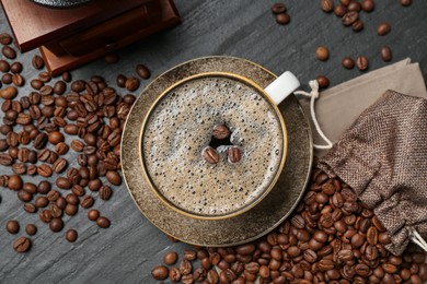 Photo of Aromatic coffee in cup, beans and grinder on black table, flat lay