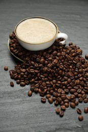 Photo of Aromatic coffee in cup and beans on black table, closeup